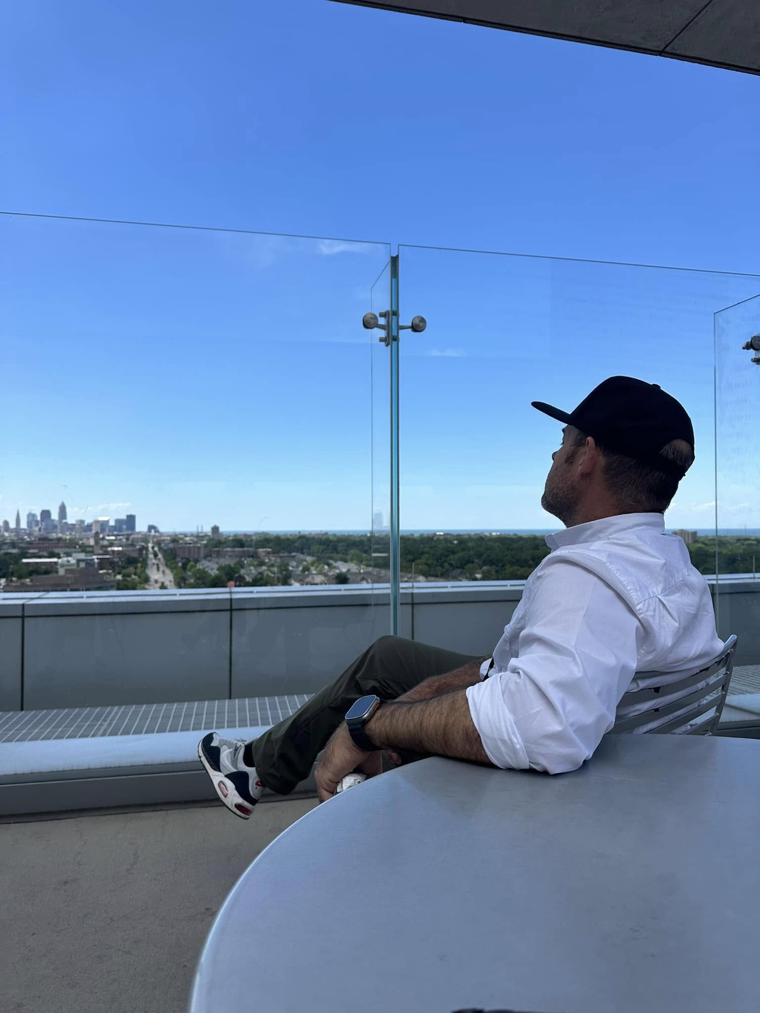 A man in his late 60s seated at a kitchen table, hand resting near his chest, contemplative.